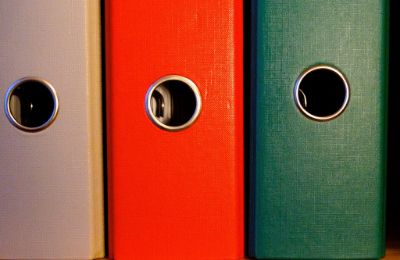 Three lever-arch files standing side by side on a shelf, in grey, red and green.
